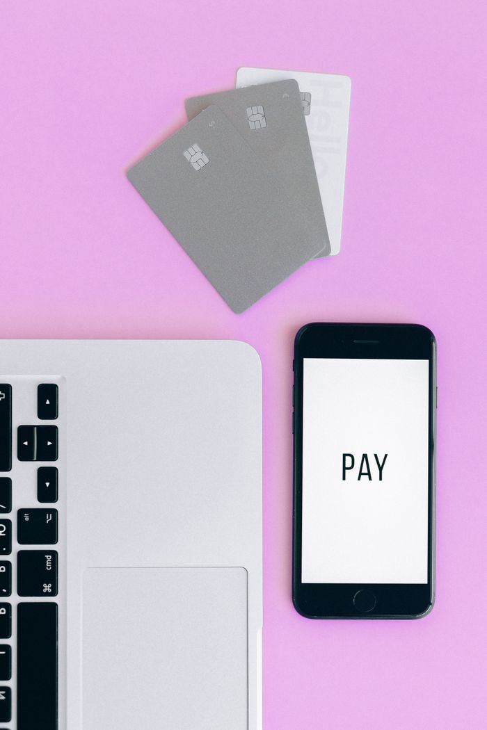 gallery-1 Overhead view of a mobile payment arrangement with a smartphone, credit cards, and a laptop on a pink background.